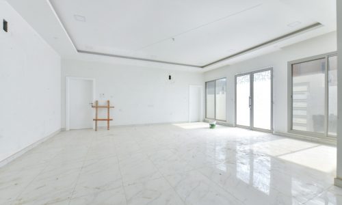 An empty room with white tile floors and sliding glass doors in an amazing villa for sale.