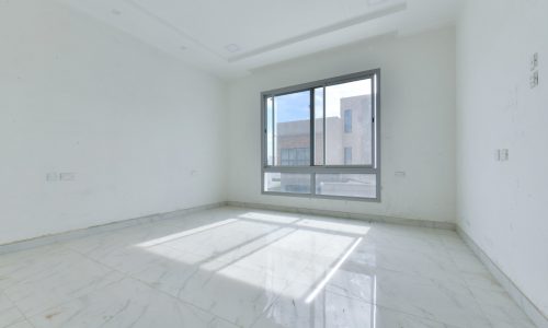 An empty room with white walls and a large window in an amazing villa for sale.