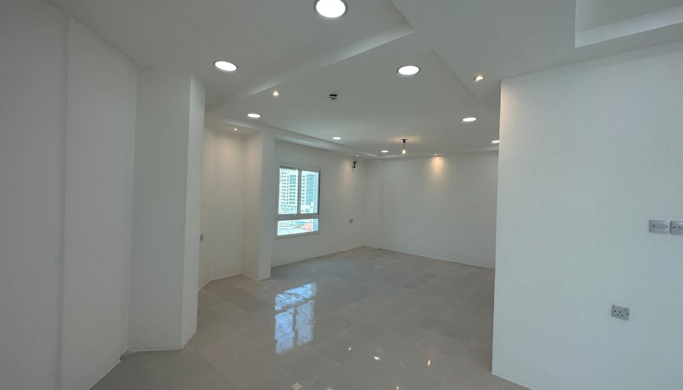 An empty room with white walls and light fixtures available for rent in Sanabis. This commercial office space is ready for occupancy.