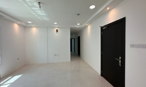 A commercial office space available for rent in Sanabis with an empty room featuring white walls and a black door.