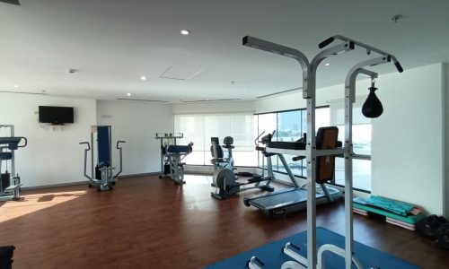 A furnished gym room with exercise equipment and a television.