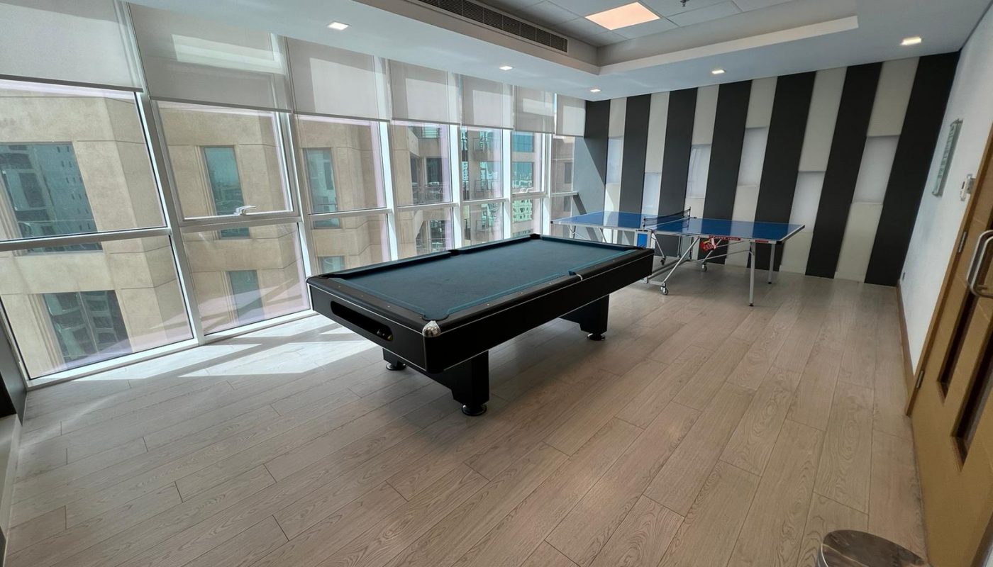 A modern game room with a pool table and a ping pong table, large windows, striped accent wall, and light wood flooring.