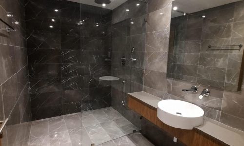 An apartment bathroom with a shower, sink and mirror offering a stunning sea view.