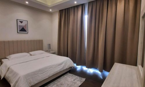 An apartment bedroom with a white bed, wooden floor, and a stunning sea view.