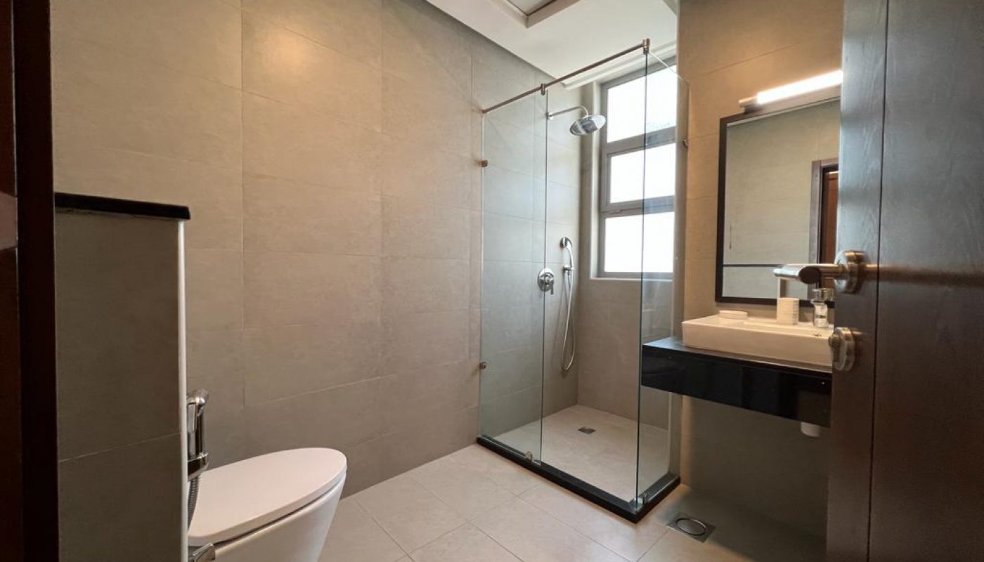 Modern bathroom with a wall-mounted toilet, glass-enclosed shower, rectangular sink, large mirror, and neutral tile walls and floor.