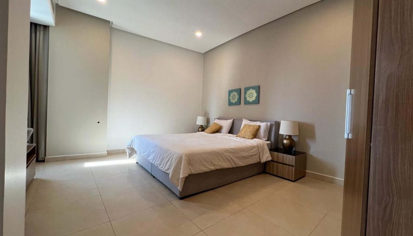 A modern bedroom with a double bed, two nightstands with lamps, tiled floor, light walls, and two decorative artworks above the bed.