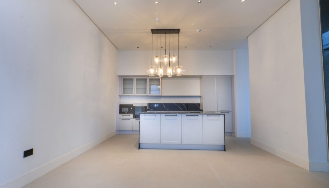 A luxuriously designed kitchen with pristine white cabinets, accentuated by a stunning chandelier.