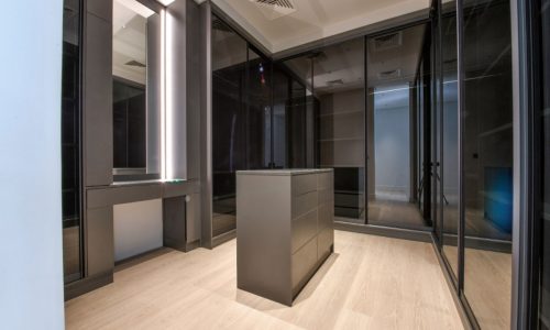 A luxurious walk-in closet in a Saar villa featuring glass doors and a wooden floor.