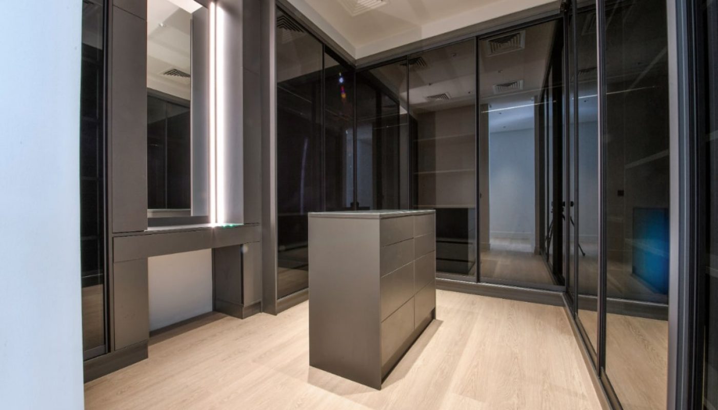 A luxurious walk-in closet in a Saar villa featuring glass doors and a wooden floor.