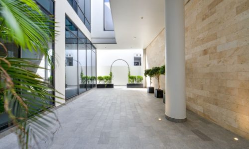 The courtyard of a modern building with large windows and plants, featuring a luxurious villa for sale.