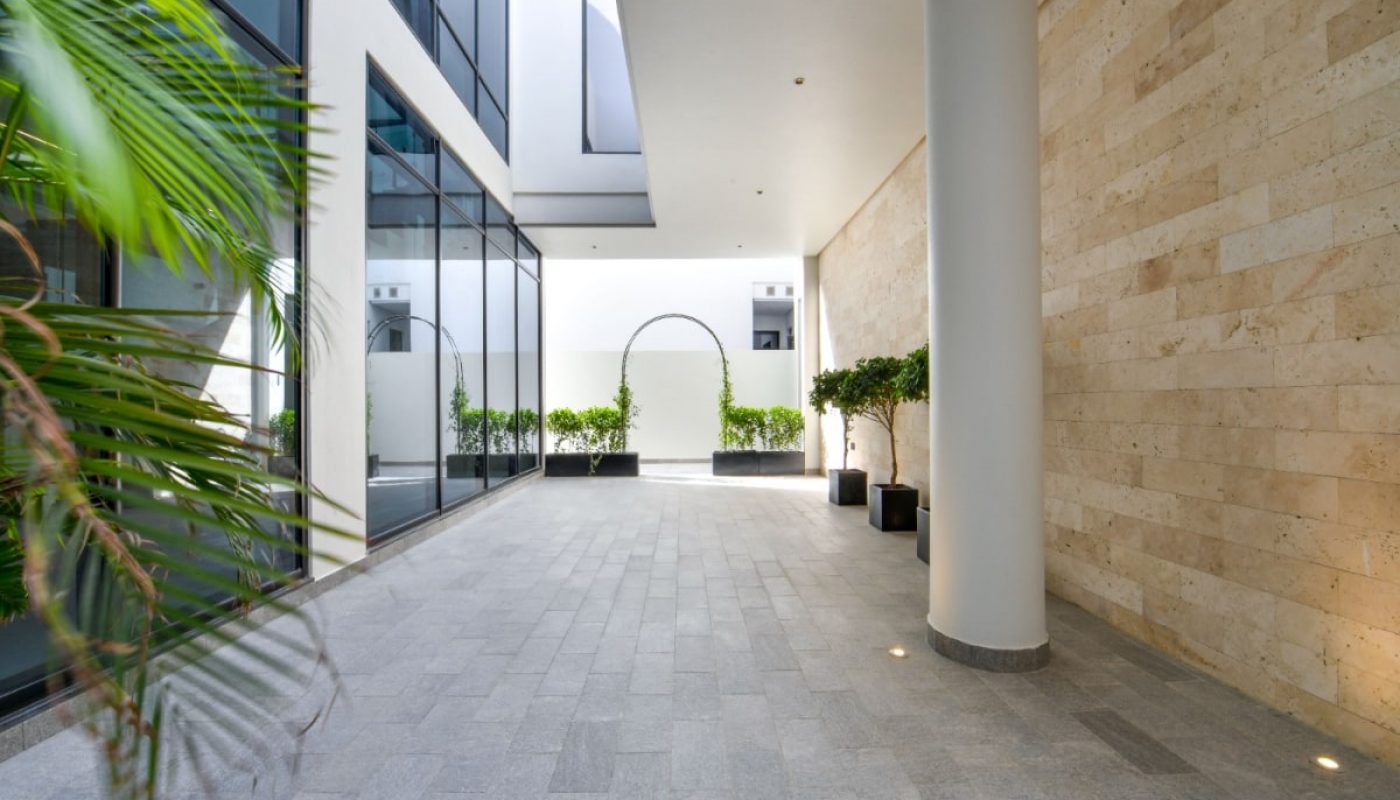 The courtyard of a modern building with large windows and plants, featuring a luxurious villa for sale.