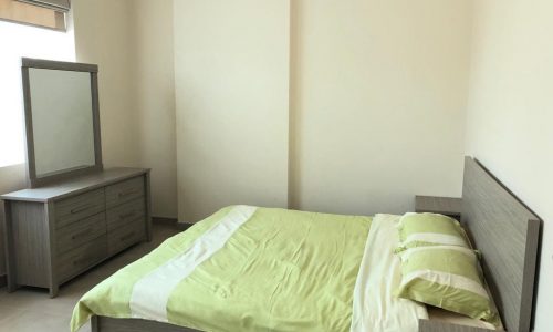 A furnished apartment in Juffair available for rent, including a bedroom with a bed, dresser, and mirror.