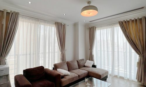 A furnished apartment in Juffair with a living room including a couch, coffee table, and curtains.