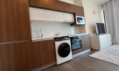 Luxury flat with a modern kitchen featuring wooden cabinets and white appliances, adjacent to a living area with a television, located in Juffair.