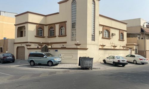 A villa for sale in Isa Town with cars parked in front of it.