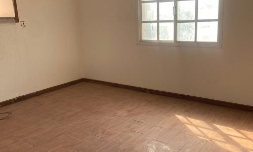 An empty villa for sale in Isa Town with wooden floors and a window.