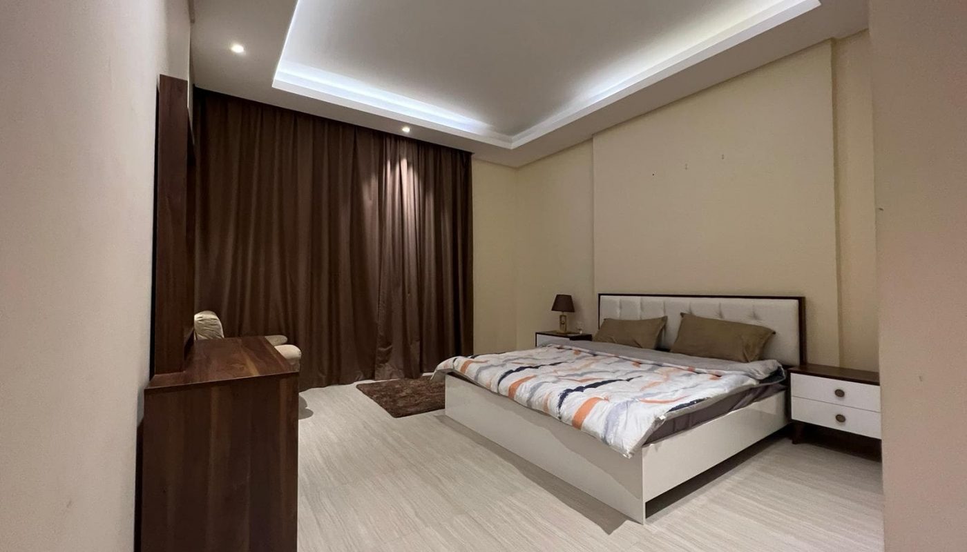 A fully furnished bedroom with a bed and a bedside table in an apartment.