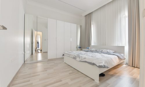 A modern villa bedroom in Janabiyah available for rent, featuring stunning wooden floors and a comfortable bed.