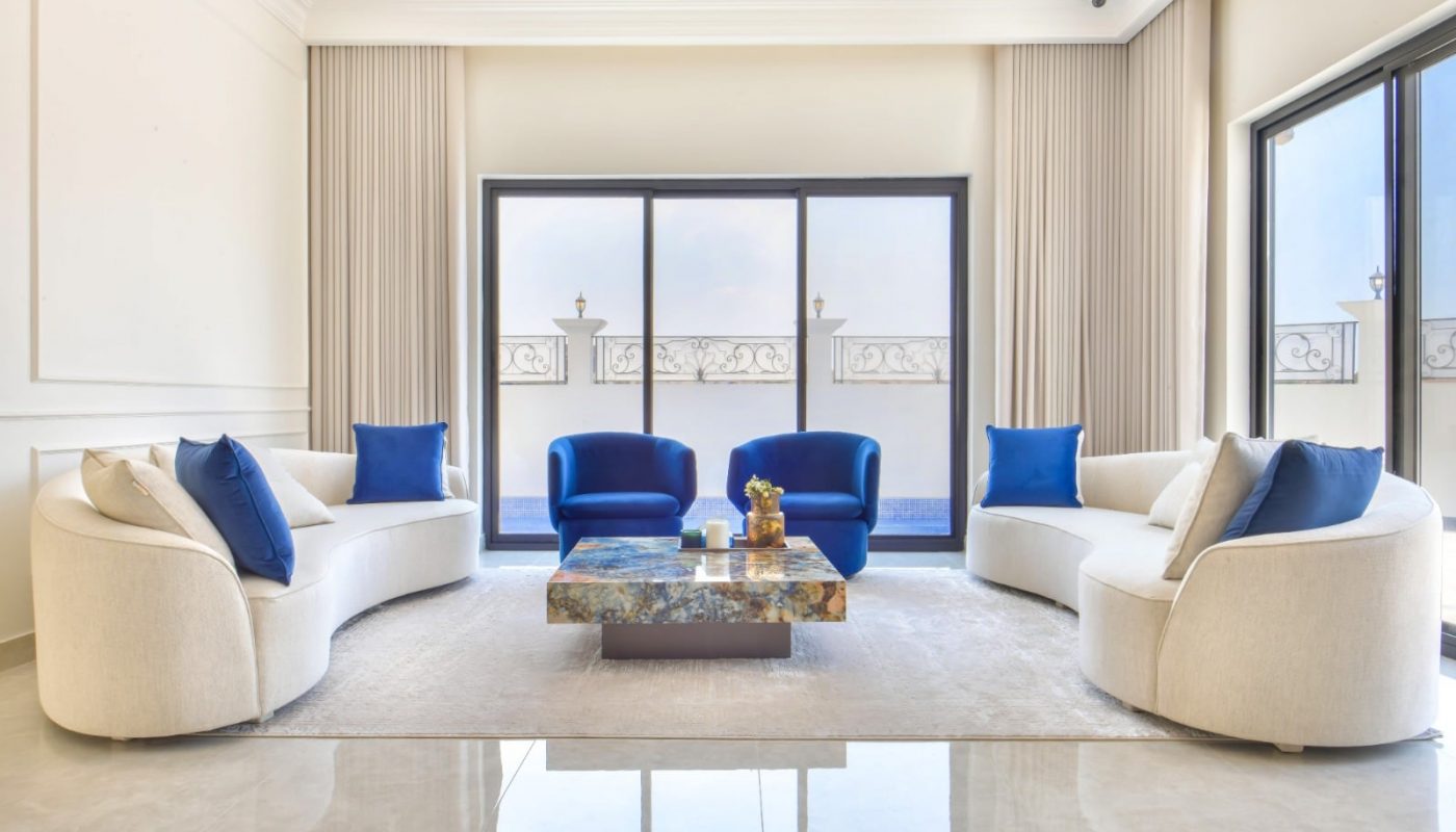 A modern villa living room in Janabiyah available for rent, featuring white furniture with elegant blue accents.