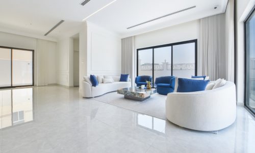 A modern villa in Janabiyah with a white living room featuring blue furniture and large windows available for rent.