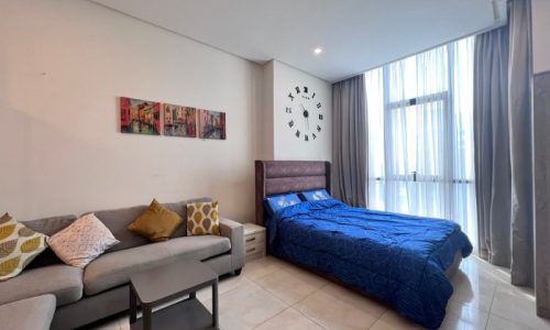 Modern bedroom in a flat for sale in Juffair, with a double bed, sofa, and wall clock.