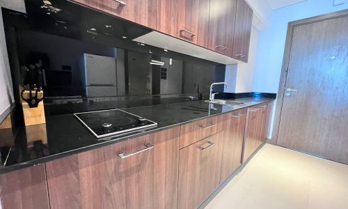 A kitchen in a luxurious residential tower adorned with wooden cabinets and black counter tops.