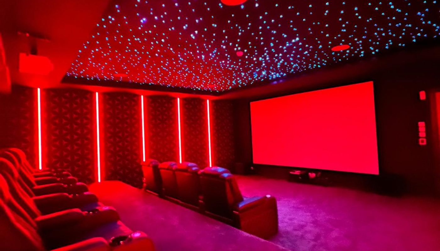 A home theater room features rows of recliner seats, a large screen, red LED wall lights, and a ceiling with blue star-like lights.