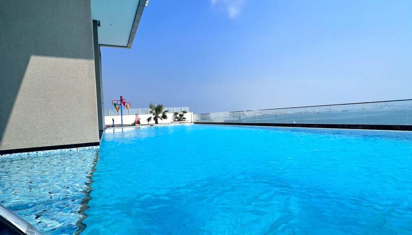A rooftop swimming pool with clear blue water, two swim rings in the foreground, and a partly cloudy sky overhead.