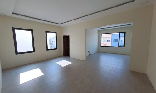 An empty room with sophisticated design, tile floors, and windows in Hamad Town villa for sale.