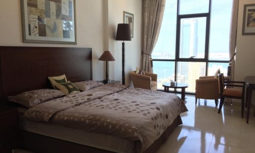 A luxury bedroom with a large bed and a view of the ocean in one of JUFFAIR's luxurious residential towers.