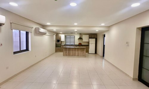 Spacious Triplex Apartment featuring an unfurnished open-plan kitchen and living area with tiled floors, recessed lighting, air conditioning units, and large windows. Perfect for those seeking a modern yet comfortable living space in Shakurah.