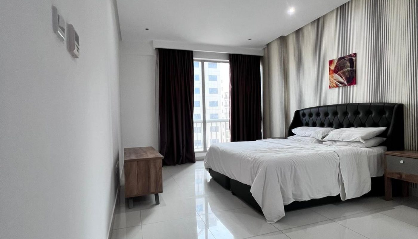 A modern bedroom with a large bed and a large window in a luxury apartment.