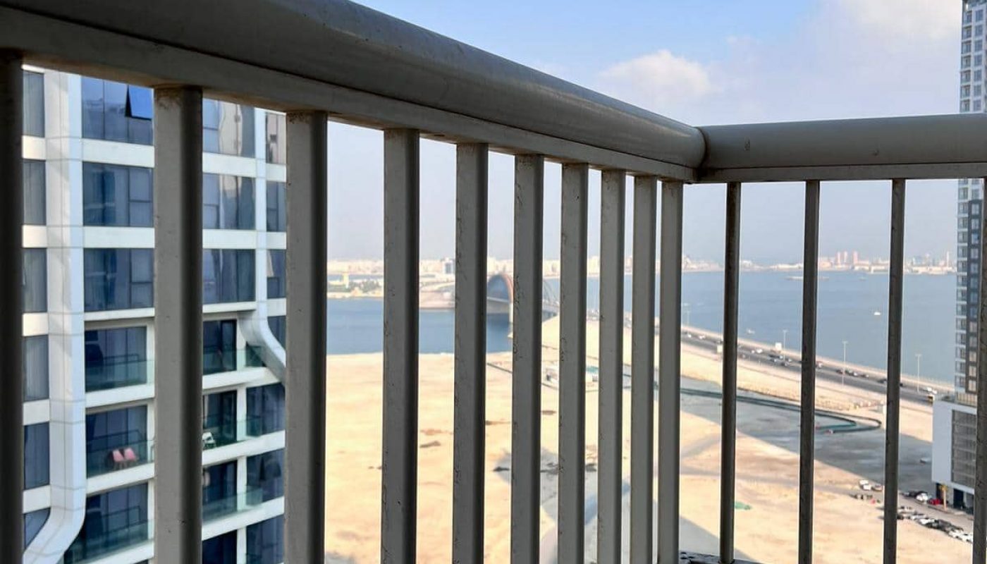 A modern apartment with a balcony offering stunning views of the water and skyscrapers.