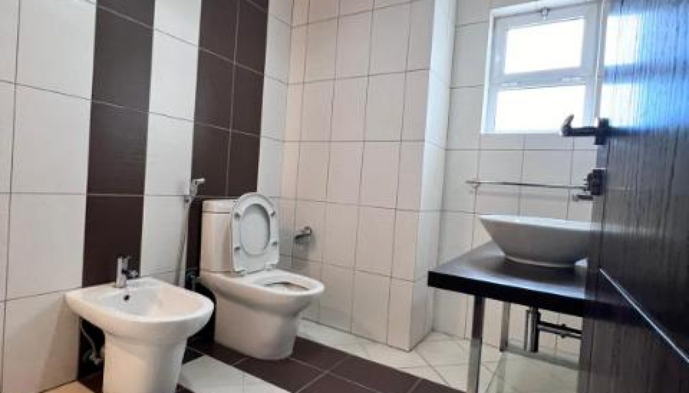 Modern bathroom with a toilet, bidet, vessel sink on a countertop, tiled walls and floor, and a window providing natural light.