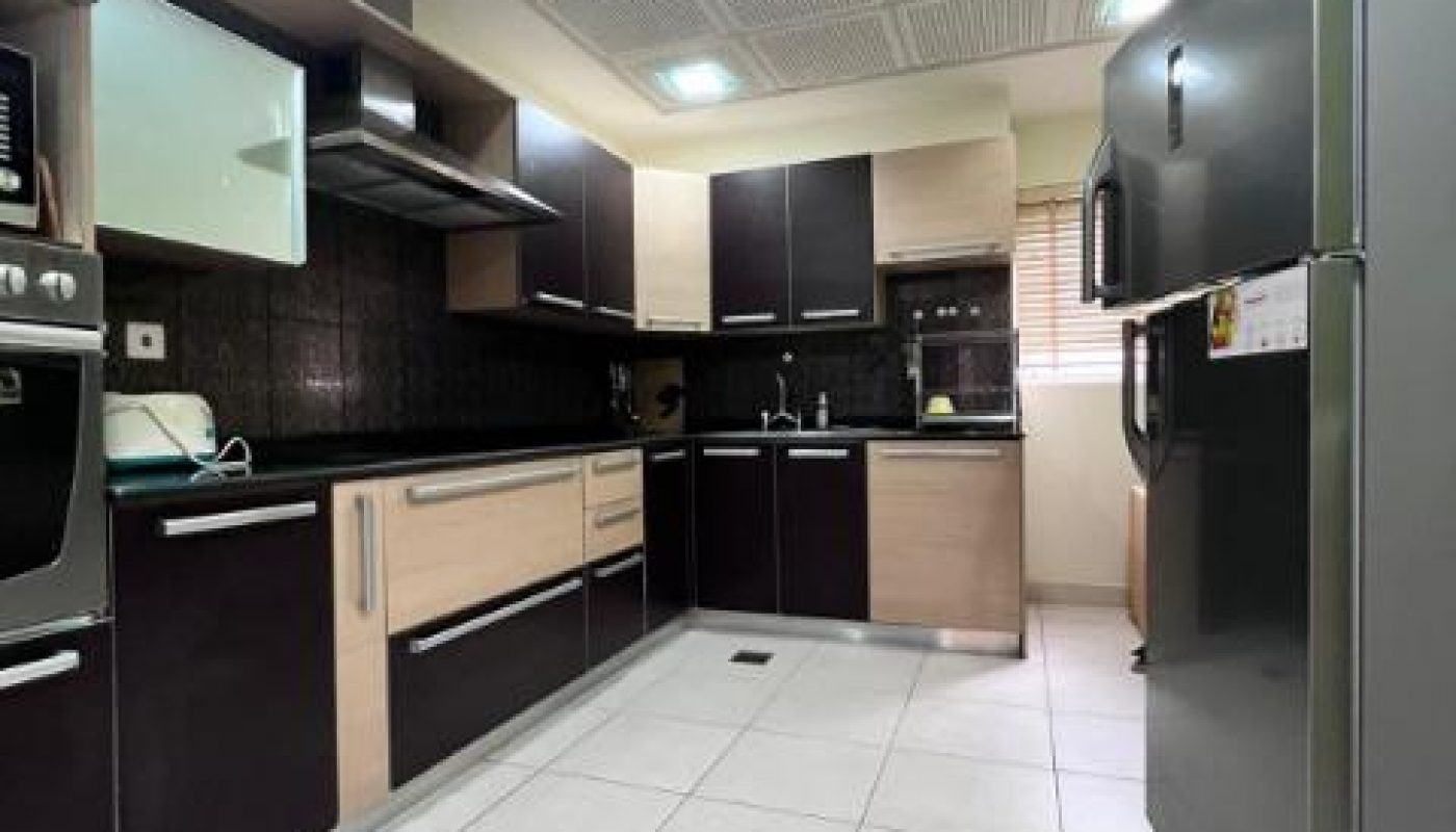 Modern kitchen with dark brown and beige cabinets, stainless steel appliances, white tiled floor, and perforated ceiling panels.