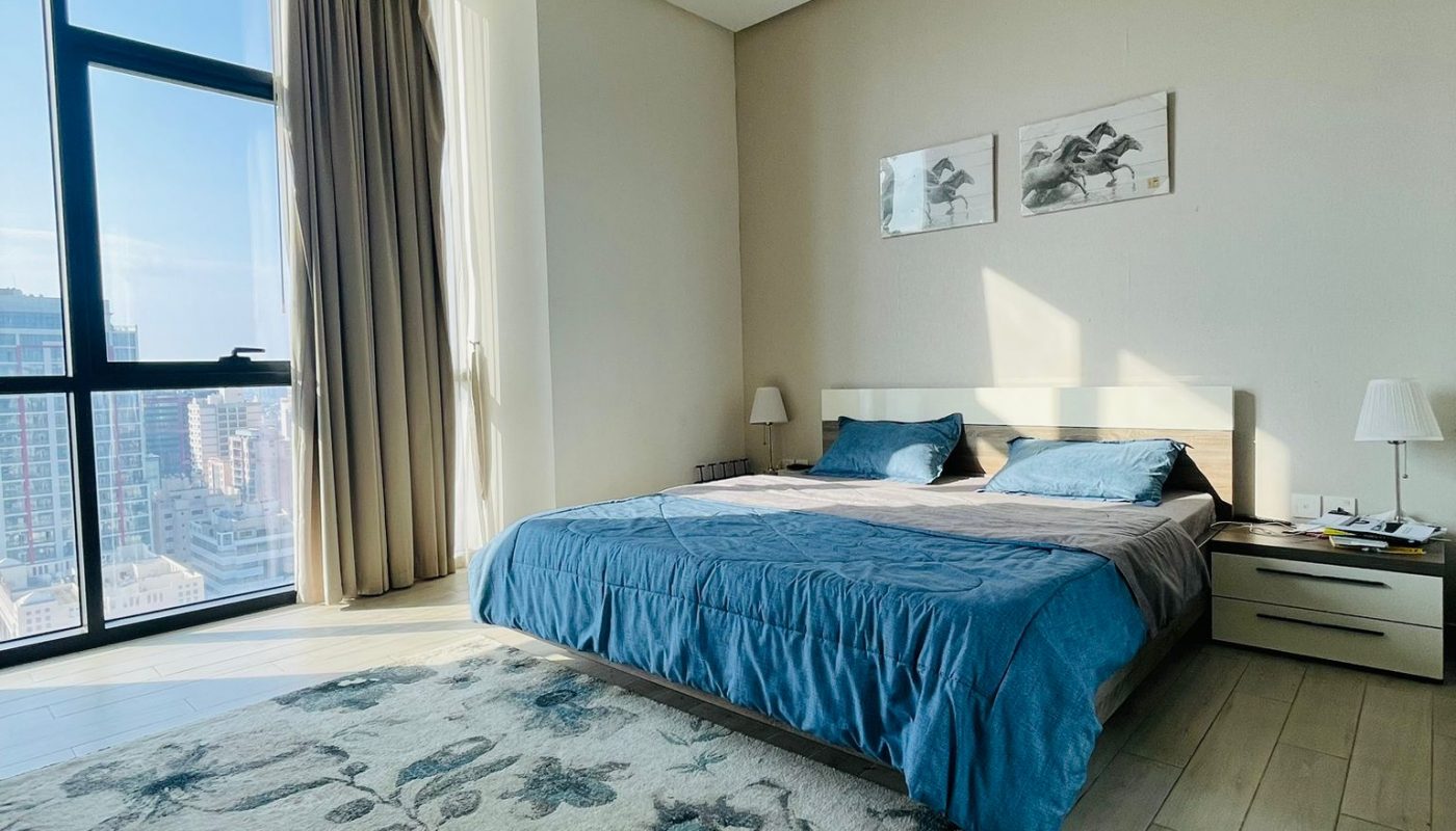 A modern bedroom in a luxury apartment with a large window overlooking the city.