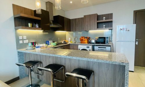 A Luxury Seef apartment with a kitchen and bar stools, equipped with a refrigerator.