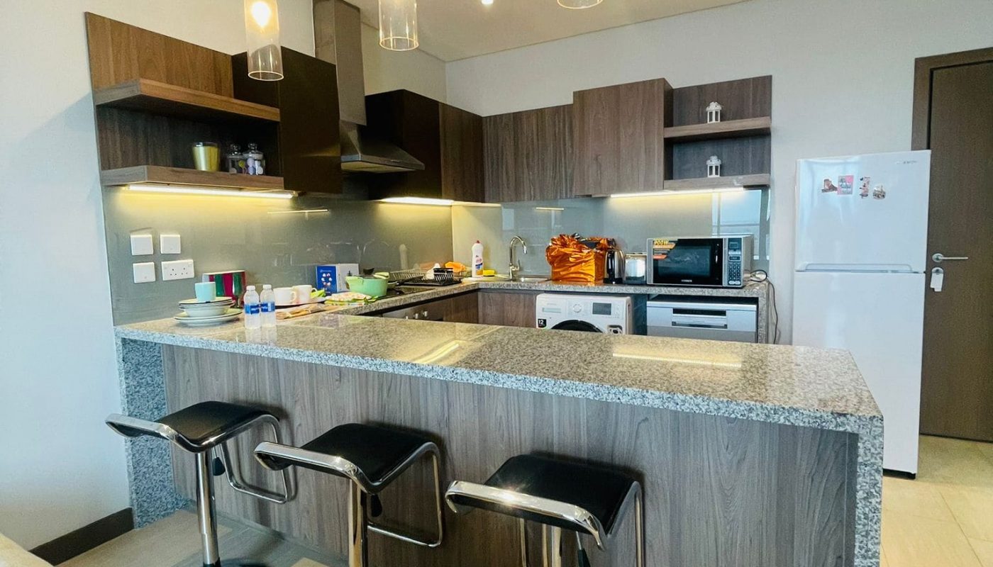 A Luxury Seef apartment with a kitchen and bar stools, equipped with a refrigerator.