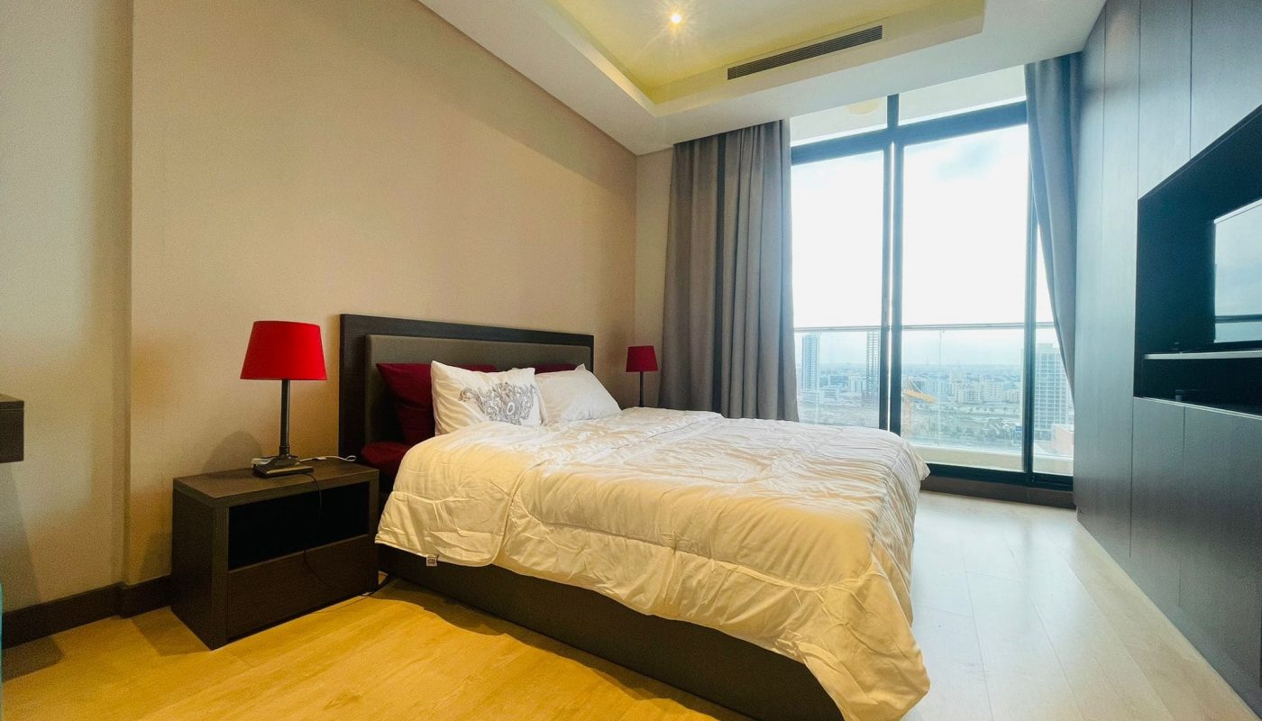 A luxury bedroom with a large bed and a flat screen TV, located in a 1 BR apartment in Seef.