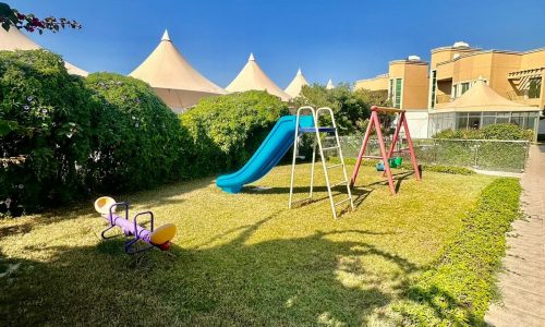 A playground with a slide and tents in the background.