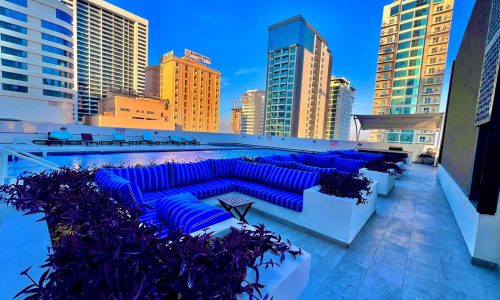 A pool with blue lounge chairs in front of luxurious residential towers.