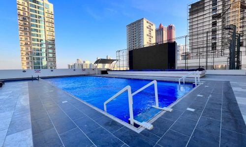 A luxurious residential tower with a swimming pool and a large screen in the background.