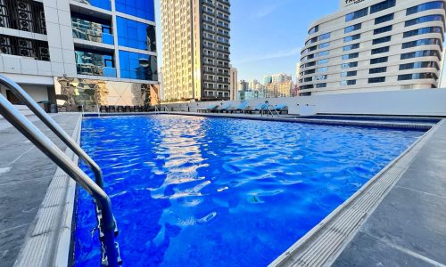 A luxury swimming pool in front of tall buildings in Juffair.