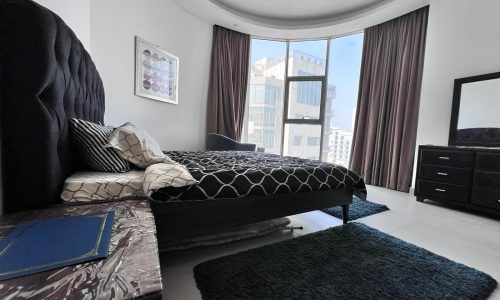 A luxurious bedroom in a city apartment with a bed, dresser, and mirror.