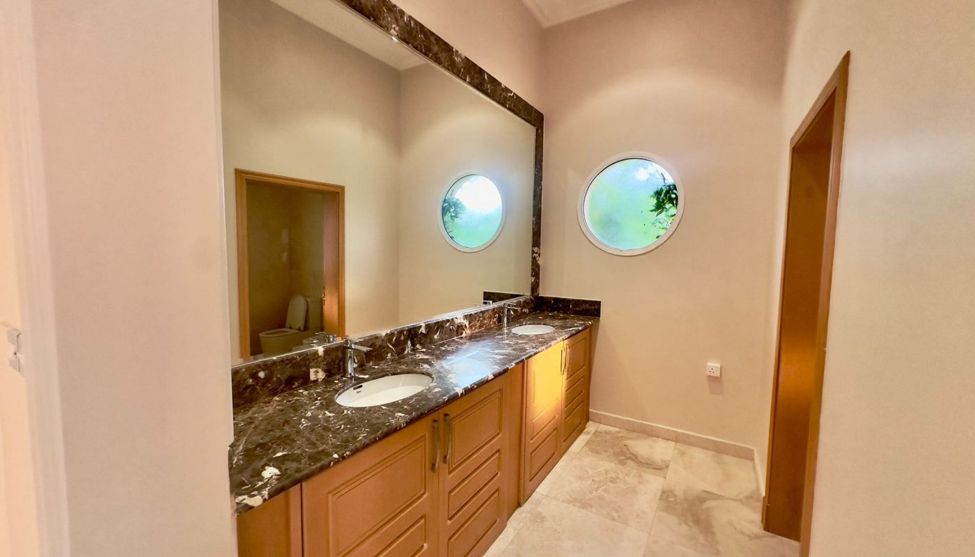 A semi-furnished bathroom in Al Janabiyah with marble counter tops and a round mirror.