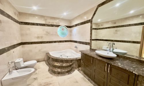 A spacious bathroom with marble floors and a large tub in a semi-furnished villa.