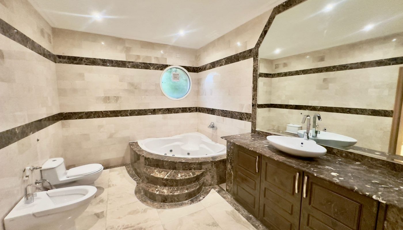 A spacious bathroom with marble floors and a large tub in a semi-furnished villa.