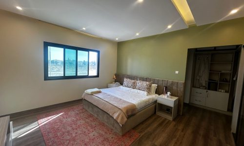 A luxury apartment in Al Janabiyah with fully-furnished 3 bedrooms, featuring green walls and a wooden floor.