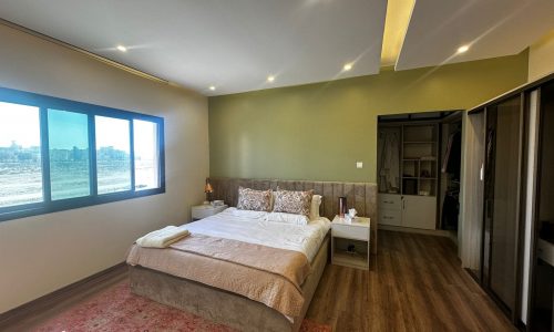 A luxury modern apartment bedroom with green walls and a wooden floor, fully-furnished in Al Janabiyah.