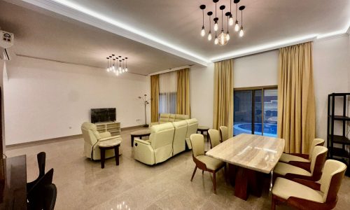 A fully-furnished living room with a dining table and chairs in a luxury villa.